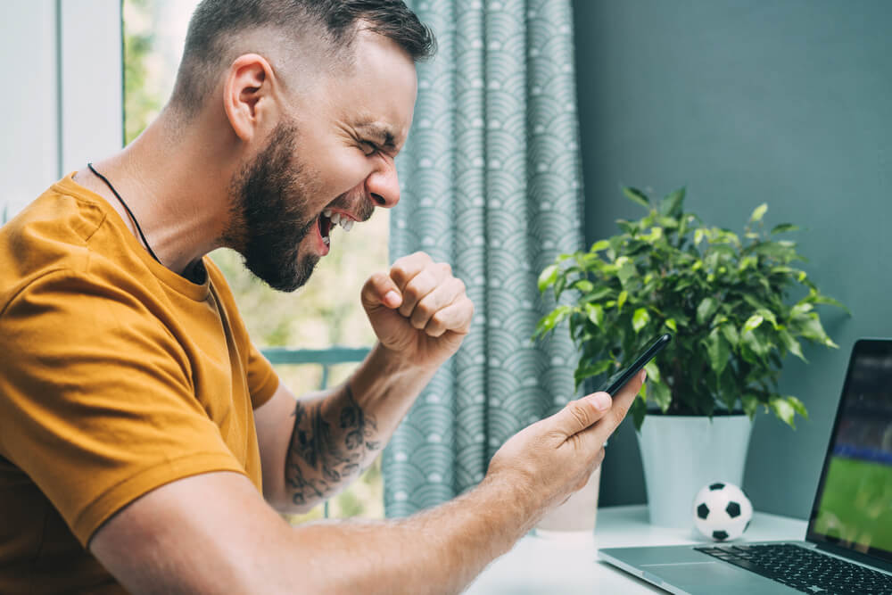 homem fazendo apostas esportivas online na betcris e comemorando